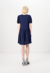 Abito corto blu navy con maniche a sbuffo, vita arricciata e orlo svasato. Il materiale sembra liscio e leggero.