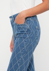 Blauwe denim jeans met diamantpatroon steentjes, vijf zakken en een getailleerde pasvorm. Gemaakt van een zachte, gestructureerde stof.