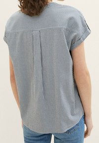 Stribet kortærmet skjorte i blå og hvid, med rund halsudskæring, detalje med rygplissé og buet søm. Tekstureret stof.