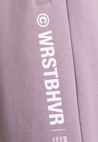 Lila Sweatshirt mit weißem Text "WRSTBHVR" und Copyright-Symbol, aus einem weichen, strukturierten Stoff und mit einem lässigen Design.
