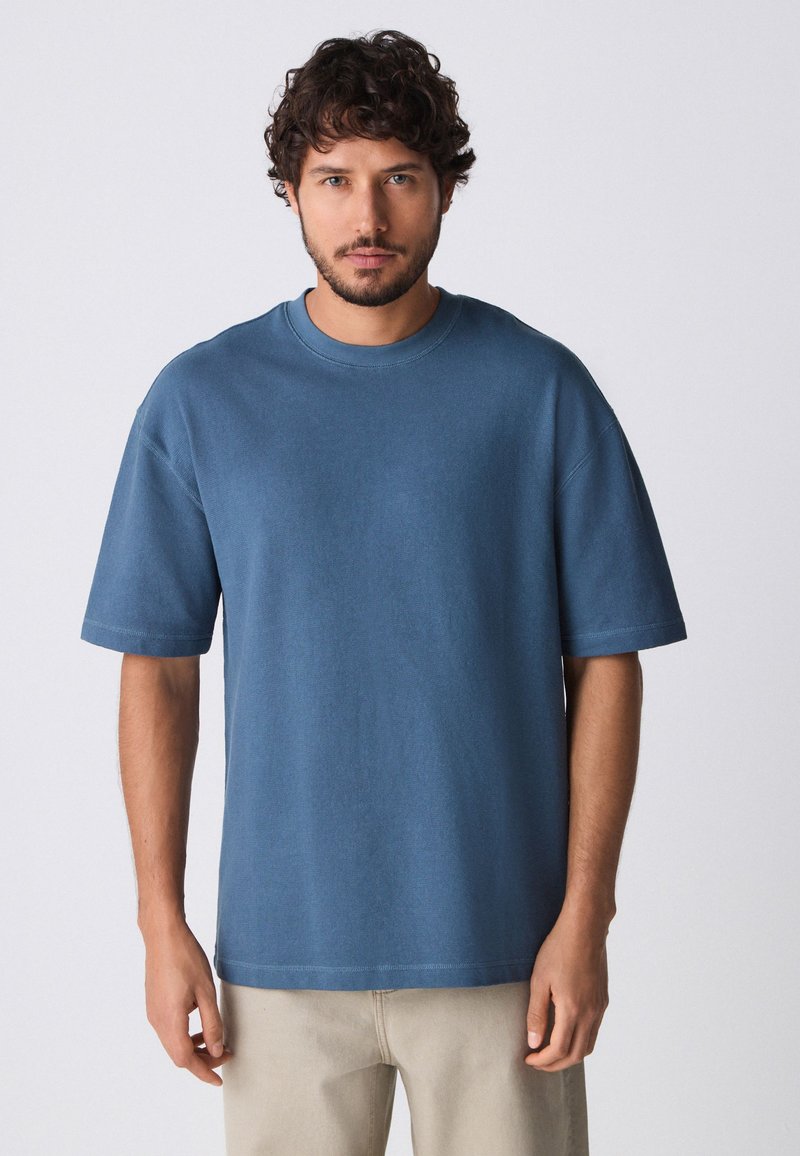 T-shirt blu a maniche corte in cotone misto con collo rotondo, vestibilità rilassata e cuciture visibili lungo l'orlo e le maniche.