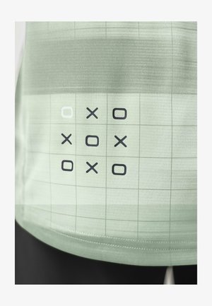 Tic-Tac-Toe-Gitter auf hellgrünem Stoff mit X- und O-Symbolen im abwechselnden Muster und einem weiß umrandeten Quadrat oben links.