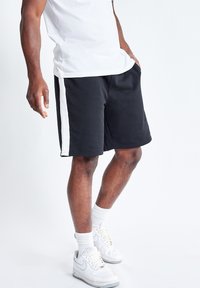 Pantalones cortos negros de tela suave, con rayas blancas en los laterales. El diseño es holgado, de longitud hasta la rodilla, con una cintura elástica.