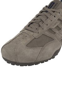 Sneaker in suede grigio con finitura testurizzata, chiusura con lacci, punta perforata e suola in gomma. Il lato presenta un design a strati e un dettaglio con logo.