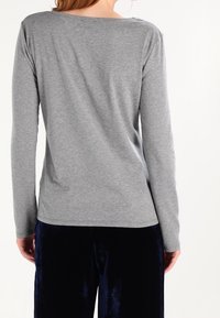 Szary longsleeve wykonany z miękkiego materiału, o luźnym kroju, z szerokim dekoltem i gładką fakturą. Połączony z ciemnymi, aksamitnymi spodniami.