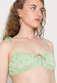 Top de biquíni floral verde com alças ajustáveis, material plissado e pequenas flores coloridas em rosa e amarelo.