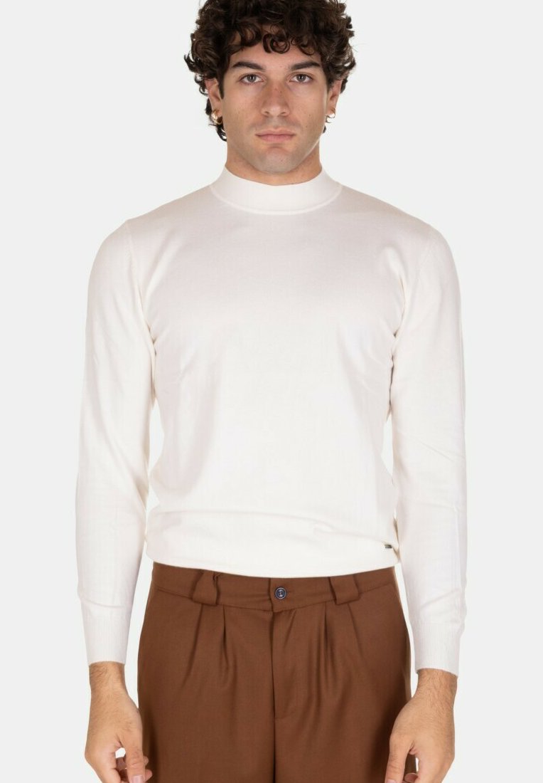 Maglione a maglia color crema con colletto alto e maniche lunghe, caratterizzato da una texture liscia e un design aderente, abbinato a pantaloni marroni su misura.
