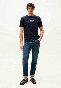 Navyblauw katoenen t-shirt met korte mouwen en een ronde hals, voorzien van een rechthoekig grafisch ontwerp in rood en blauw aan de voorkant, gecombineerd met een blauwe spijkerbroek.