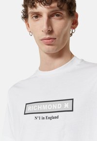 T-shirt in cotone bianco con grafica rettangolare nera contenente il testo "RICHMOND" e "N°1 in Inghilterra" in colori a contrasto.