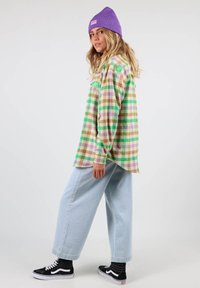Chemise en flanelle à carreaux multicolores dans les tons vert, violet et marron ; associée à un jean baggy bleu clair et des baskets noires avec des accents blancs.