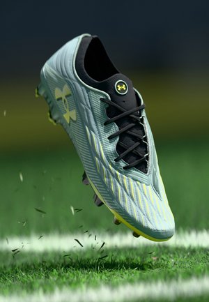 Scarpe da calcio verde chiaro con un design testurizzato, lacci neri e logo Under Armour. Presentano accenti gialli e un motivo in rilievo sulla parte superiore.