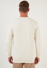 Heren sweatshirt van crème, geweven stof, lange mouwen, ronde halslijn, elastische manchetten en zoom, eenvoudig ontwerp zonder zichtbare branding of patronen.