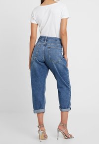 Džínové kalhoty středně modré barvy s volným střihem, vysokým pasem, ohrnutými nohavicemi a zadními kapsami. Spárovány s bílým tričkem a stříbrnými sandály na podpatku.