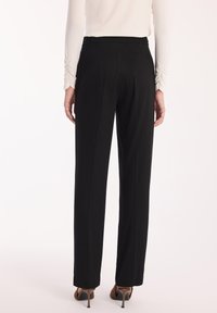 Tylny widok osoby w czarnych prostych spodniach, białej bluzce z długim rękawem i brązowych butach na obcasie, na białym tle.