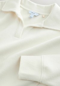 Maglione bianco con texture a coste, colletto classico e mezza chiusura a bottoni. Etichetta con la scritta "NEXT". Tessuto morbido e leggero.