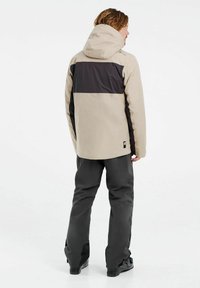 Beige en zwarte waterdichte jas met een capuchon, met een gestreept ontwerp en verstelbare manchetten, gecombineerd met donkere broeken.