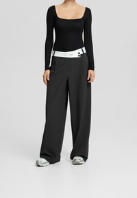 Svart långärmad bodysuit med fyrkantig halsringning, tillsammans med högmidjade vida byxor med vit midja och två knappar.