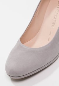 Chaussure à talon haut en suede gris avec un bout arrondi et un décolleté bas, dotée d'une doublure intérieure lisse et d'une marque discrète embossée sur la semelle intérieure.