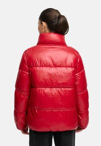 Giacca a vento rossa con colletto alto, design trapuntato e materiale lucido. Maniche ampie e vestibilità rilassata, con dettagli di cucitura orizzontale.