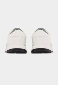 Λευκά sneakers χαμηλού τύπου, εμφανιζόμενα από πίσω, με μαύρες σόλες και το λογότυπο "Calvin Klein" σε κάθε πτέρνα.