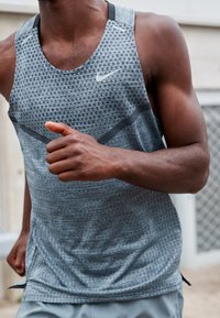 Débardeur athlétique gris léger avec un motif texturé. Présente un col rond et des fentes latérales pour plus de mobilité. Logo sur la poitrine.