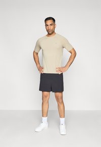 Beige sportpóló, rövid ujjú, könnyű anyag; fekete sorttal párosítva, sima textúrájú; fehér sportcipő szalaggal és bokazokni.