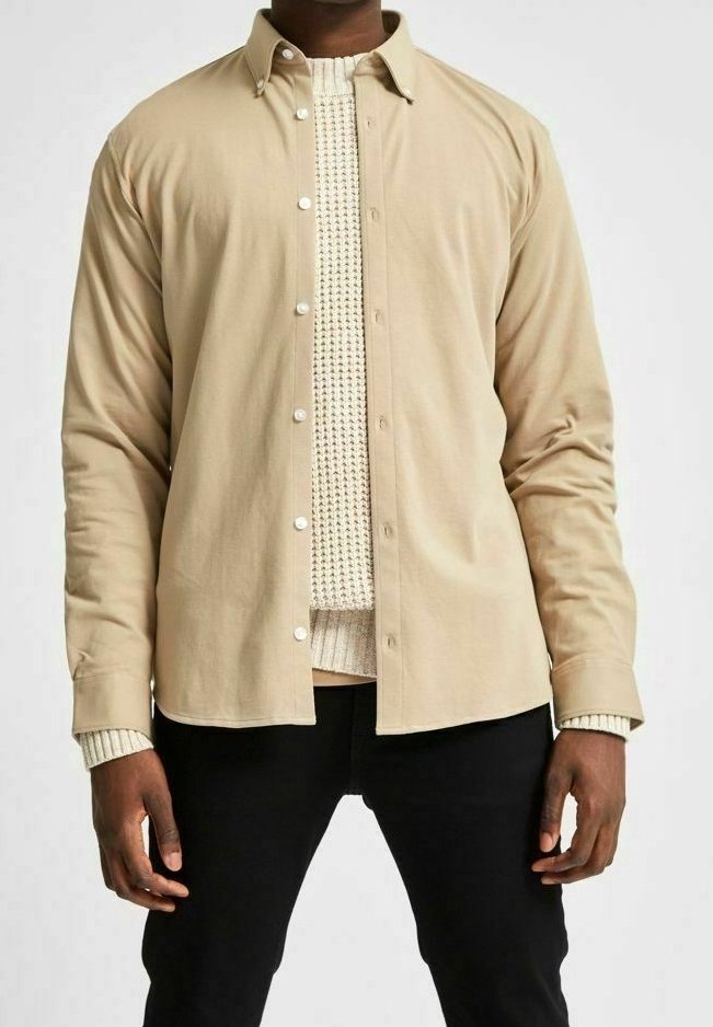 Beige knapplångärmad skjorta gjord av mjukt tyg med en slät yta, prydd med vita knappar och en klassisk krage, överlagd på en krämfärgad stickad tröja.