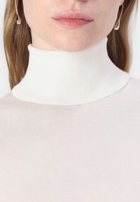 Hvitt ribbet høyhalset genser med en tettsittende design, som har en glatt tekstur og en høy hals. Subtil, lys rosa under.