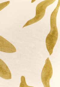 Beige tyg med en slät textur som har abstrakta olivgröna vågiga former och mönster, vilket skapar en dynamisk visuell effekt.