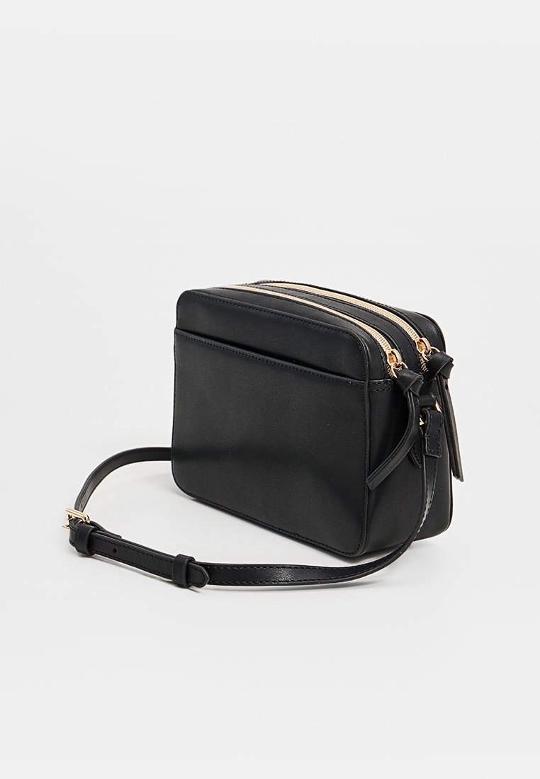 Bolso cruzado de cuero negro con dos cremalleras superiores, correa ajustable, bolsillo frontal plano y detalles en tono dorado. Textura suave.