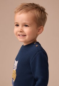 Jersey de punto azul marino con diseño de oso, cuello redondo y botones de madera en el hombro, con tejido texturizado y detalles coloridos.