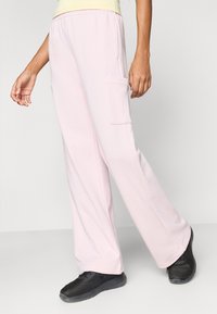 Ροζ ανοιχτόχρωμο παντελόνι με φαρδιά μπατζάκια από απαλό ύφασμα, με πλαϊνή τσέπη. Συνδυασμένο με μαύρα αθλητικά από δίχτυ για αντίθεση.