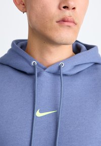 Felpa con cappuccio Nike in tessuto blu chiaro, caratterizzata da una tasca anteriore, un cordino e un piccolo logo verde neon sul petto.
