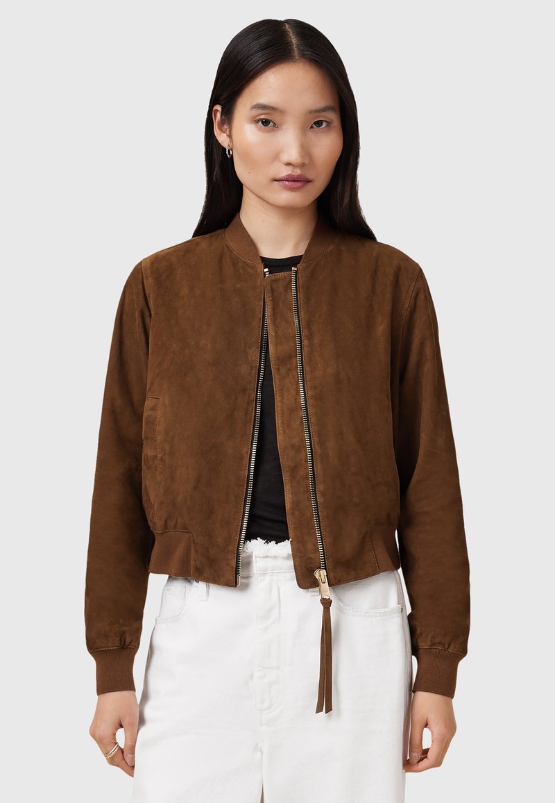 Giacca bomber in suede marrone con zip frontale, polsini e vita a costine. Presenta tasche laterali e un dettaglio decorativo con nappina sulla zip.
