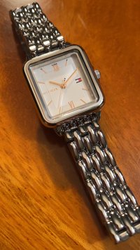 Monitorius kvadratinio forma sidabro atspalvio su balta tekstūruota ciferblatu, rožinio aukso rodyklėmis ir grandinėlės apyranke. Pasižymi romėniškais skaičiais ir prekės ženklo logotipu.