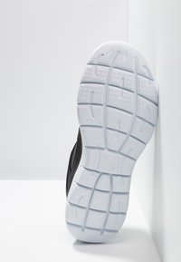 Black athletic shoe with a textured mesh upper and a white rubber sole featuring deep treads for grip on various surfaces.