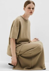 Kaki-farvet oversized t-shirt og matchende vide bukser i et glat stof. Toppen har korte ærmer og en rund halsudskæring.