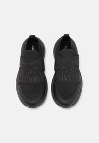Scarpe nere con tomaia in rete e dettagli in pelle testurizzata. Presentano cinturini con logo finiti in opaco e un design a punta arrotondata.