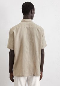 Camicia a maniche corte di un beige chiaro con righe bianche verticali. Tessuto morbido, design casual, dettaglio colletto e orlo dritto.