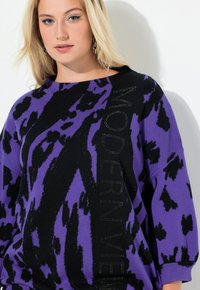 Czarny i fioletowy, oversize'owy sweter ze zwierzęcym nadrukiem, ozdobiony dekoracyjnym napisem "MODERN VIEW" z błyszczącymi akcentami wzdłuż jednej strony.