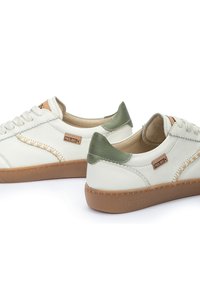 Baskets en cuir blanc avec des accents verts au talon et une étiquette en suède beige. Comprend des coutures beiges, des lacets ronds et des semelles en caoutchouc.
