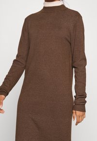 Abito lavorato a maglia marrone con maniche lunghe, colletto alto e polsini a coste. Texture liscia con una leggera lucentezza.