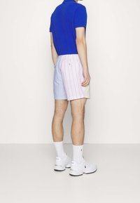 Camisa polo azul para hombre combinada con pantalones cortos a rayas de colores pastel. Zapatillas blancas y calcetines hasta el tobillo completan el look.