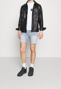 Chaqueta de cuero negra, camiseta blanca con un logo, pantalones cortos de mezclilla clara rasgados, calcetines blancos y zapatillas negras.