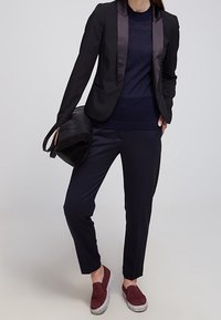 Svart blazermed satängslag, marinblå tröja, skräddarsydda marinblå byxor och vinröda slip-in skor. Accessoar: svart axelväska.