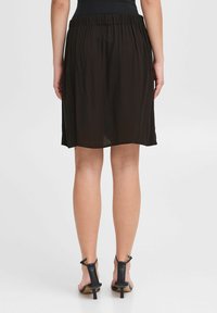 Gonna nera midi con vita elastica arricciata e tessuto leggero e fluido. Indossata con sandali con tacco neri e cinturini.