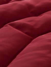 Bordeauxroter Steppbett mit glatter Textur, versehen mit parallelen Nählinien und einem weichen, plüschigen Design.