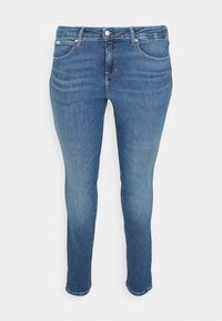 Jeans ajustados en denim azul medio con cinco bolsillos, ligeros desvanecimientos, costuras visibles y cierre de botón con cremallera.