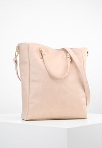 Jasnoróżowa torba typu tote ze skóry z dwoma uchwytami i odpinanym paskiem na ramię. Posiada elementy w odcieniu złota oraz gładkie, matowe wykończenie.