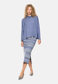 Hellblaues, langärmliges Oberteil mit lockerem Schnitt und Tasche, kombiniert mit einem gemusterten, knielangen Rock mit blauen und weißen kreisförmigen Designs.